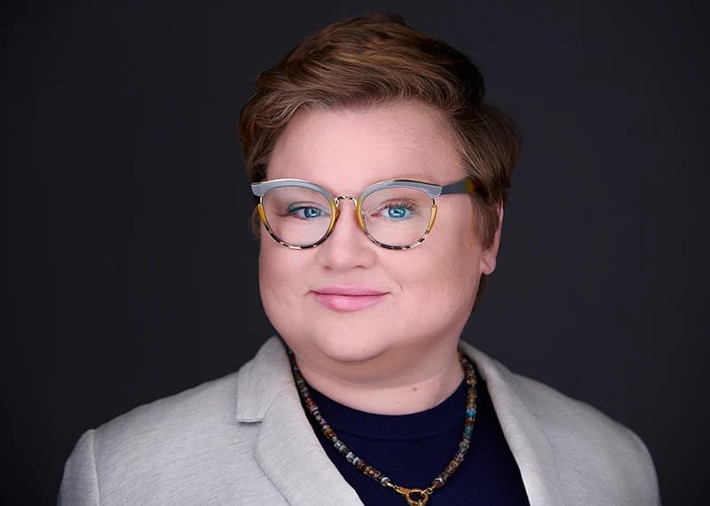 Professional headshot on dark background - woman in gray blazer