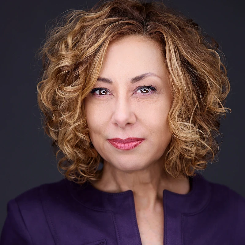 Fun headshot of a white college director with curly blonde hair, bright red lipstick, and a stylish purple top, radiating enthusiasm in Pittsburgh PA.