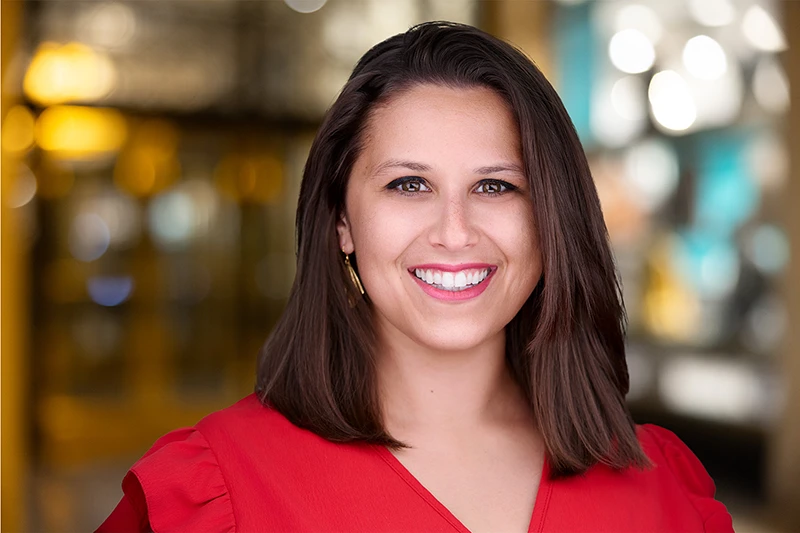 headshot of smiling woman in red suit with office background