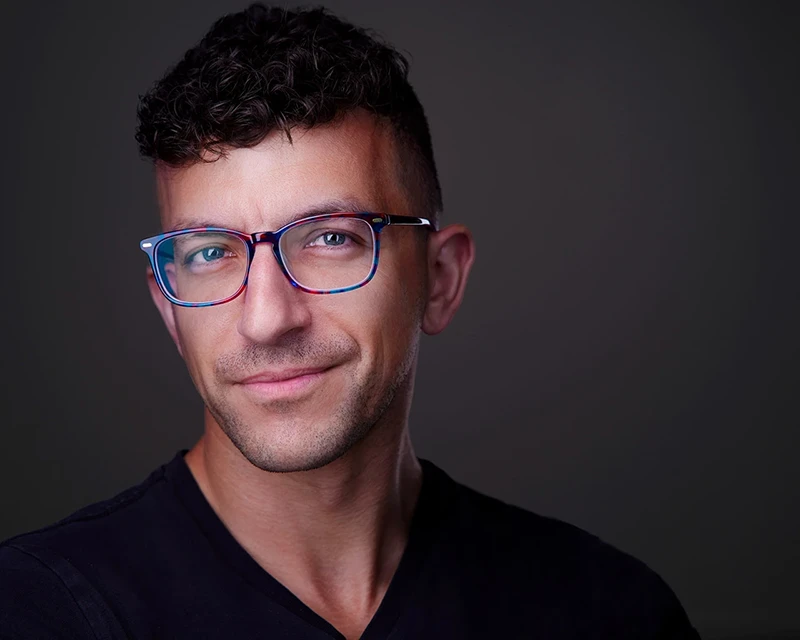 Headshot of Chad Isaiah, a renowned headshot photographer in Pittsburgh, wearing blue and purple glasses and displaying a warm, professional smile