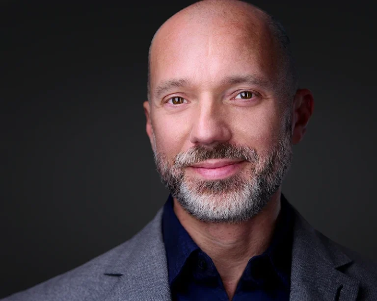 headshot of man with white beard in a blue shirt and gray jacket