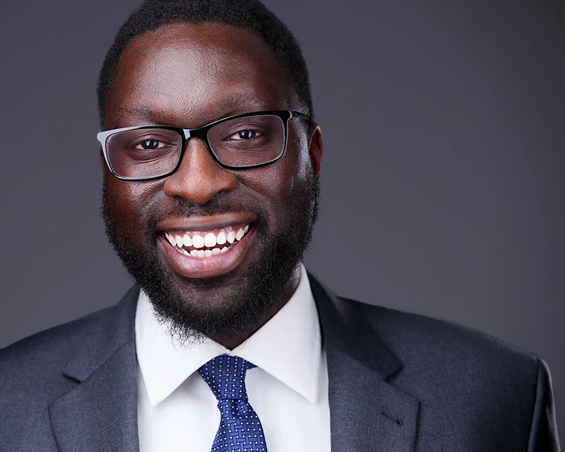 Professional headshot of a smiling black male attorney dressed in a stylish gray suit and a blue tie