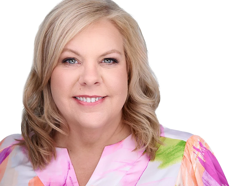 headshot of woman with blonde hair in floral shirt on white background