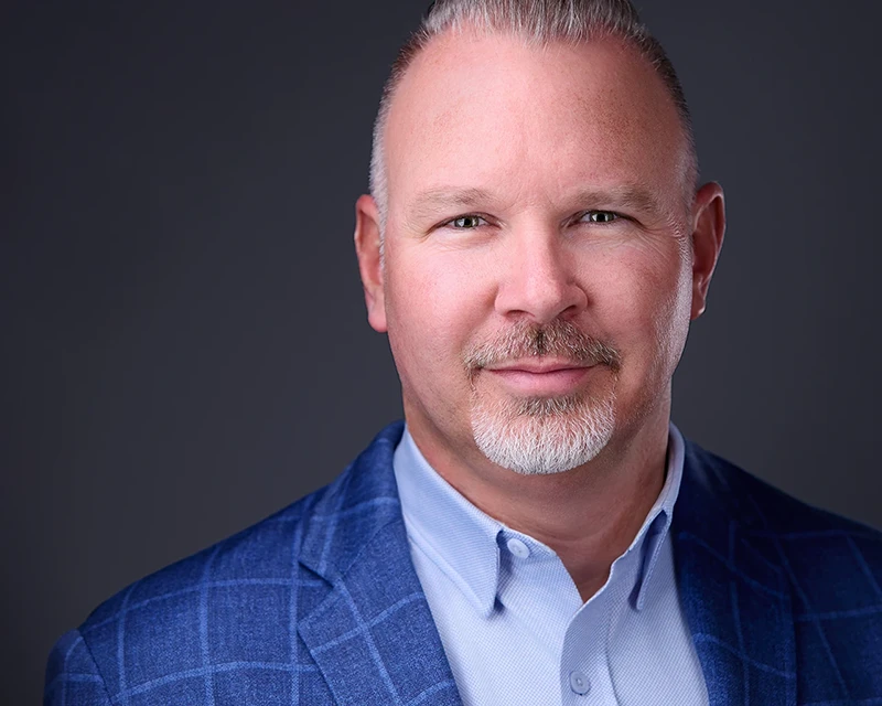 grinning headshot of man with white beard in a blue shirt and blue suit