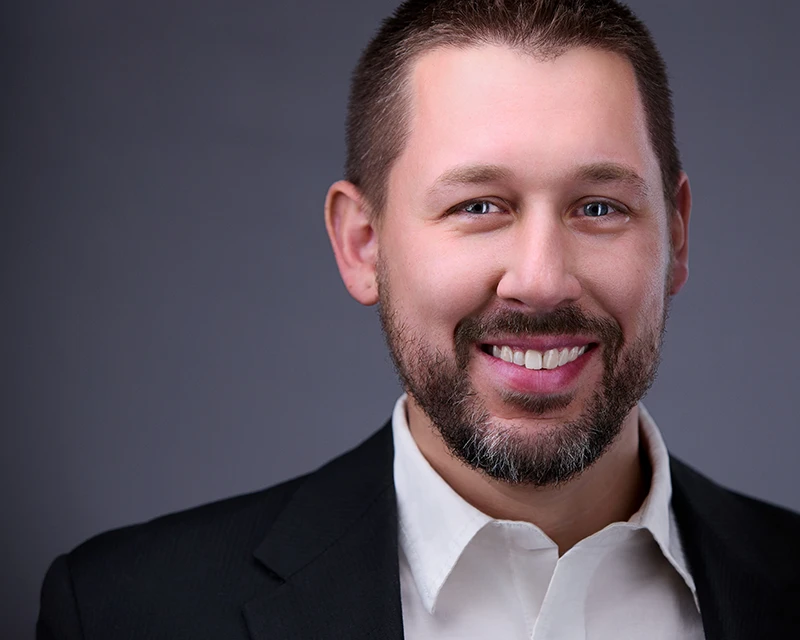 Approachable C-level executive sporting short beard, radiating confidence in pristine white shirt and polished black jacket