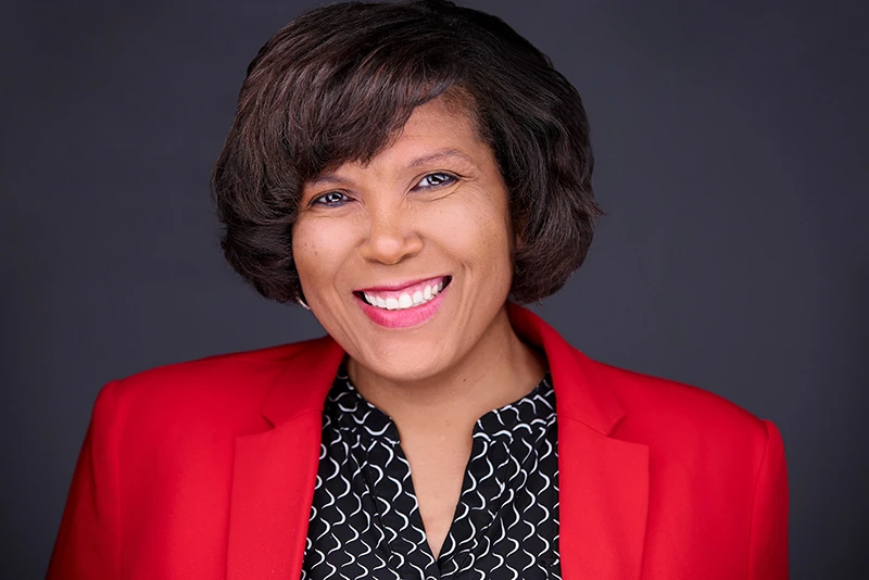 Confident black businesswoman Traci Jackson smiling in vibrant red jacket and patterned shirt